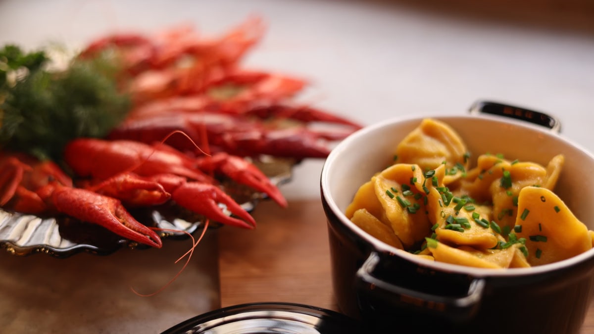 Appetizing crayfish and tortellini dish served in a ceramic pot, garnished with chives.